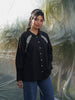 Woman wearing a black shirt with white embroidery standing against a transparent backdrop.