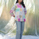 Woman wearing a colorful checkered shirt and jeans standing in front of a translucent fabric backdrop.
