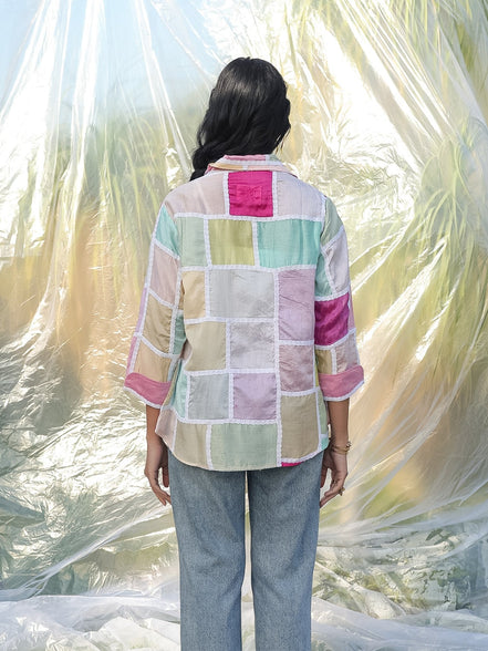 Person wearing a colorful patchwork shirt and jeans standing in front of a textured white fabric.