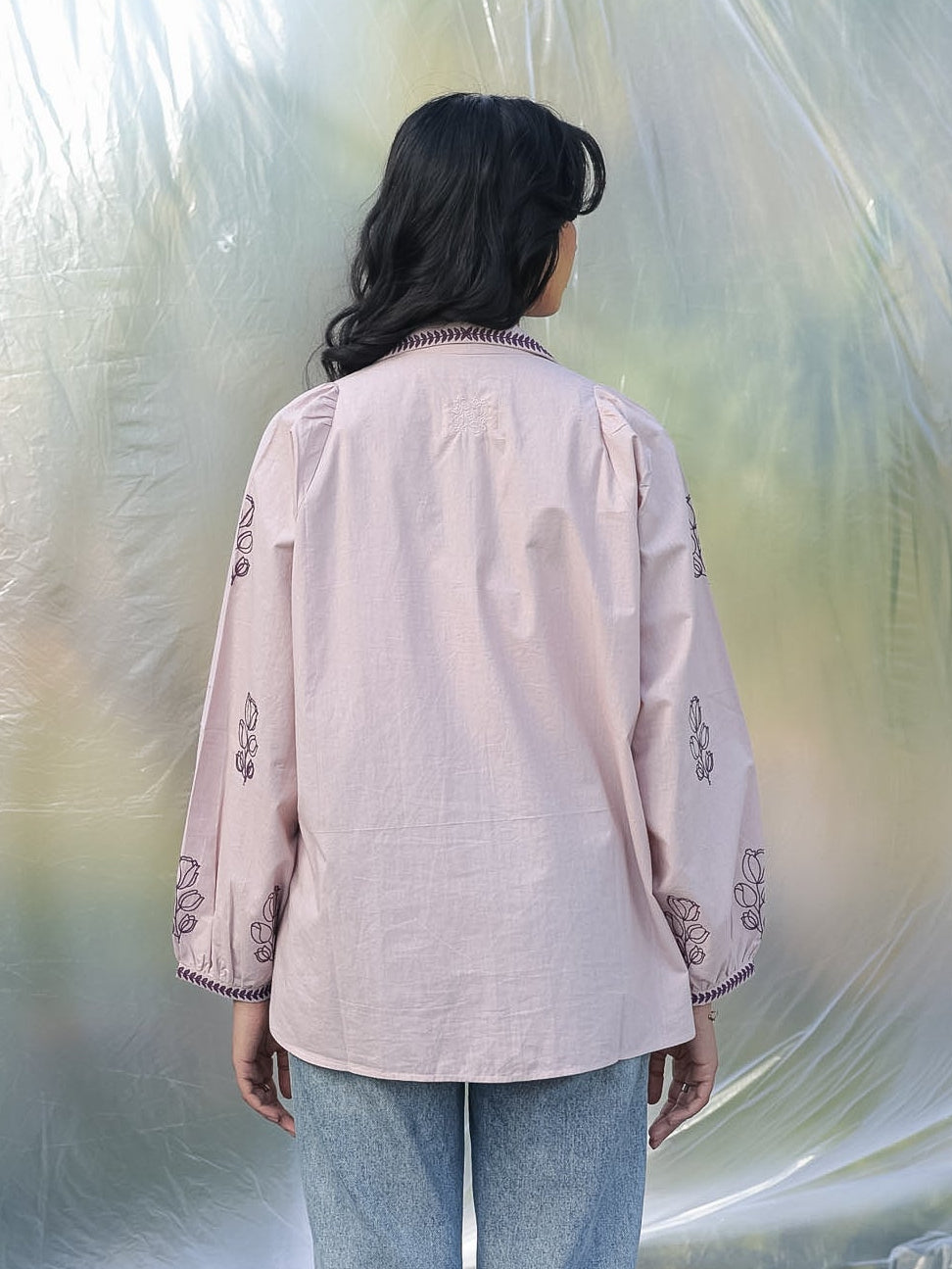 Person wearing a light pink embroidered shirt and blue jeans standing inside a large plastic bubble.