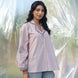 Woman wearing a light pink embroidered shirt with blue jeans against a blurred natural background