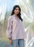 Woman wearing a light pink embroidered shirt with blue jeans against a blurred natural background