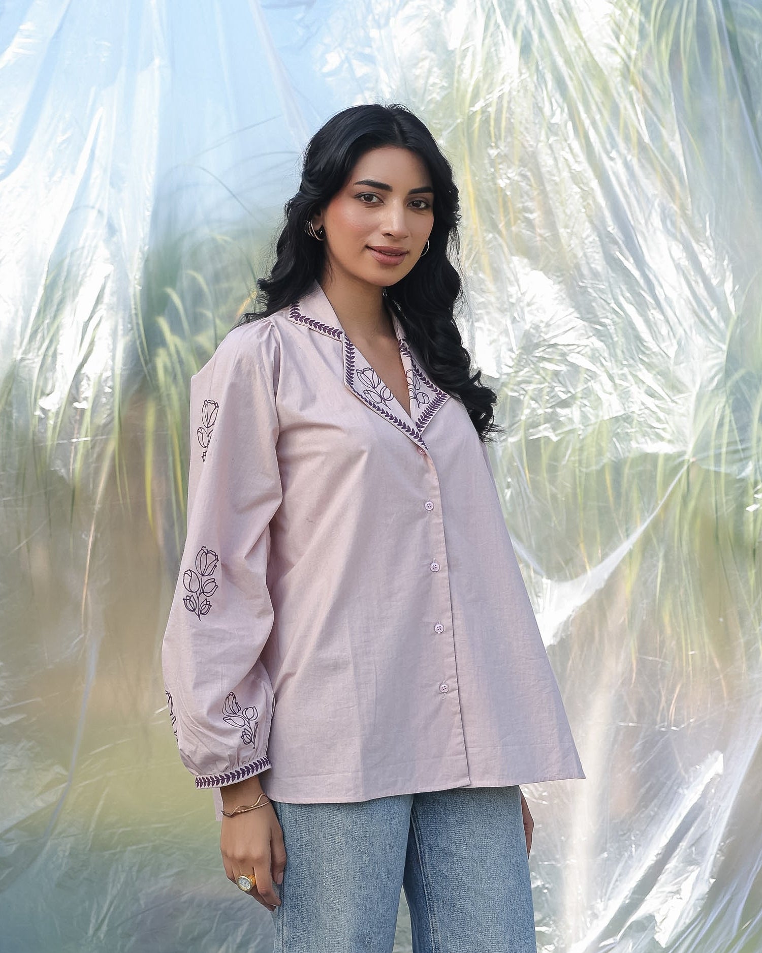 Woman wearing a light pink embroidered shirt with blue jeans against a blurred natural background