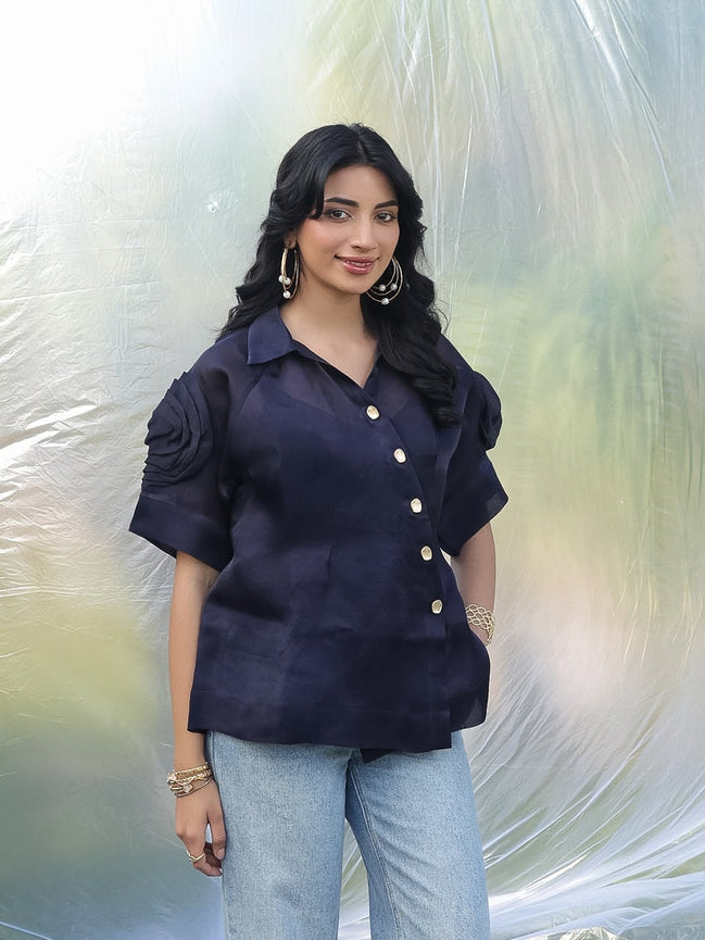 Woman wearing a dark blue blouse with ruffled sleeves against a light background