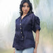 Woman wearing a dark blue blouse with short sleeves against a blurred natural background