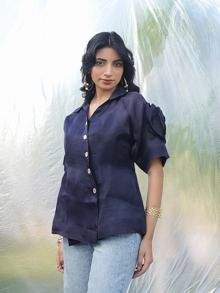 Woman wearing a dark blue blouse with short sleeves against a blurred natural background