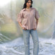Woman wearing a cold coffee shirt and light blue jeans standing against a textured white background