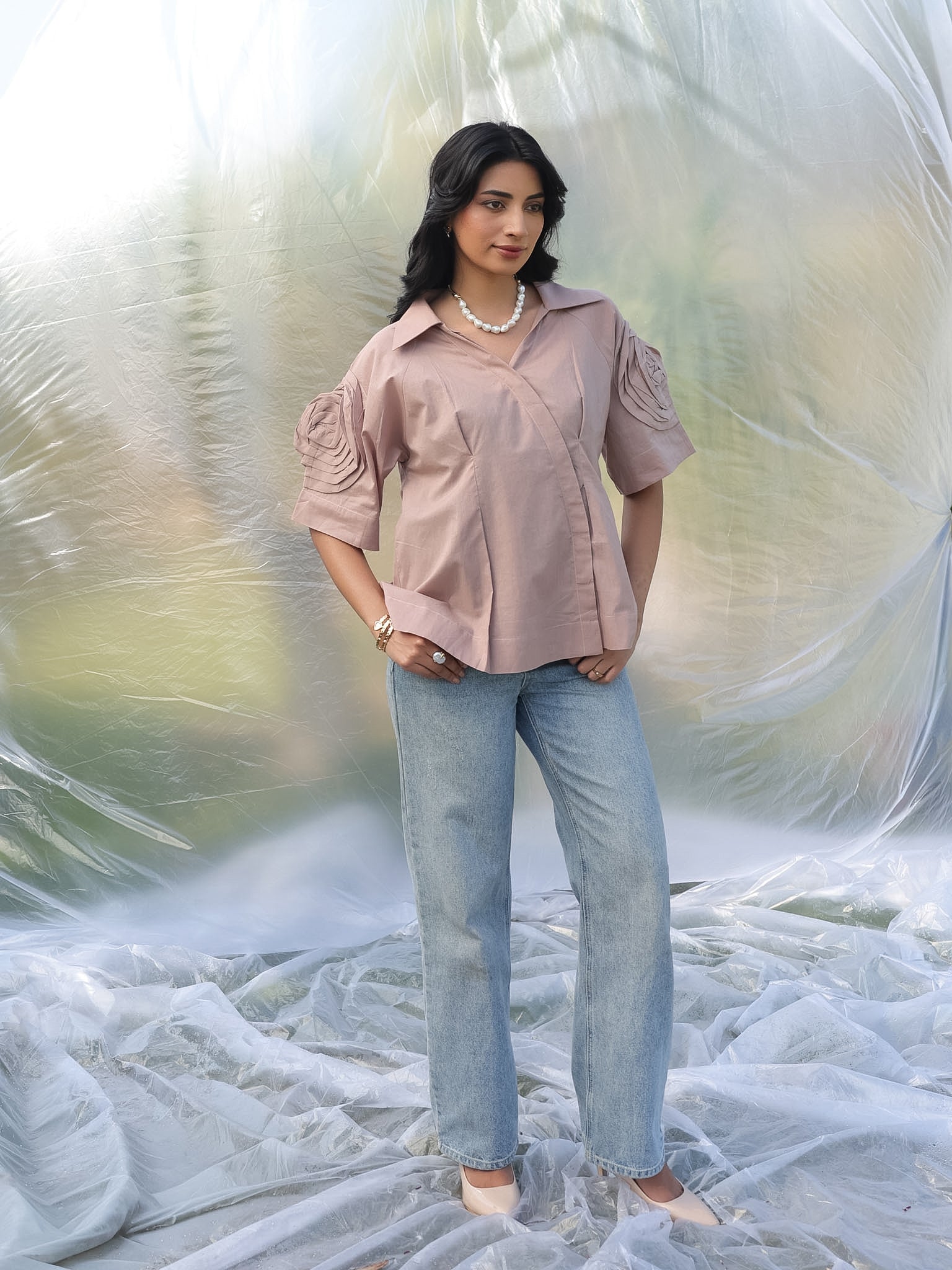 Woman wearing a cold coffee shirt and light blue jeans standing against a textured white background