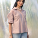 Woman wearing a party wear beige shirt and light blue jeans standing against a blurred natural background