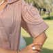 Close-up of a person wearing a beige short-sleeve shirt with rose sleeves with a blurred outdoor background