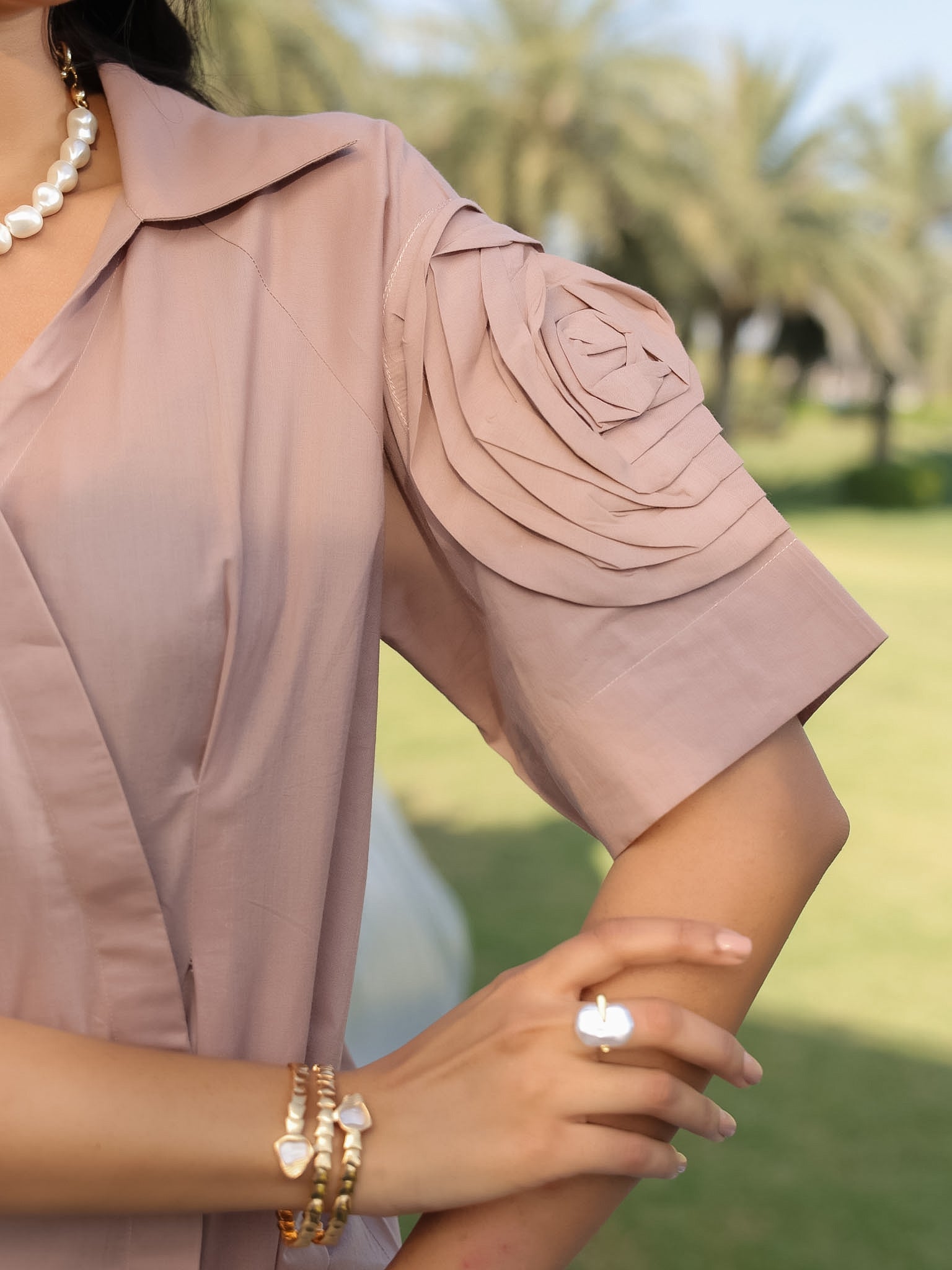 Close-up of a person wearing a beige short-sleeve shirt with rose sleeves with a blurred outdoor background