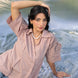 Woman in a cold coffe shirt with high fashion sleeves, sitting on a textured surface.