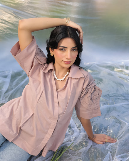 Woman in a cold coffe shirt with high fashion sleeves, sitting on a textured surface.