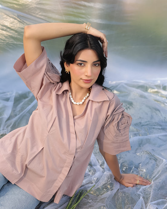 Woman in a cold coffe shirt with high fashion sleeves, sitting on a textured surface.