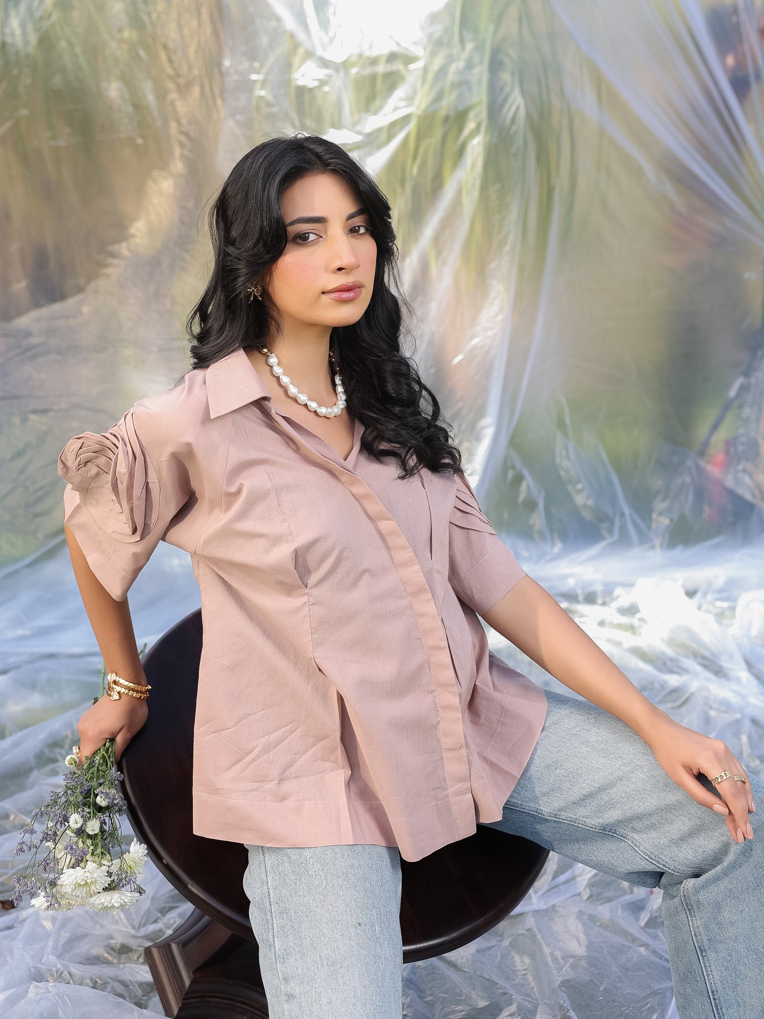 Woman in abrown shirt and jeans sitting on a chair with a blurred natural background