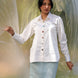 Woman wearing a white shirt and light blue skirt standing in front of a translucent curtain.