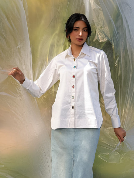 Woman wearing a white shirt and light blue skirt standing in front of a translucent curtain.