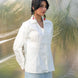 Woman wearing a white shirt and light blue skirt standing in a natural setting with greenery.