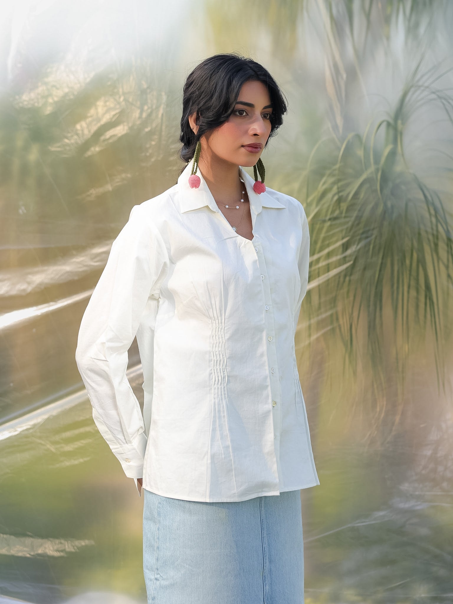 Woman wearing a white shirt and light blue skirt standing in a natural setting with greenery.