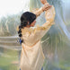 Woman in a beige shirt and blue pants standing in front of a blurred natural background