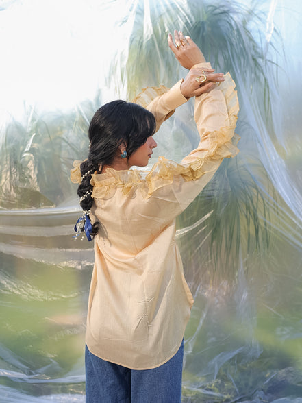 Woman in a beige shirt and blue pants standing in front of a blurred natural background