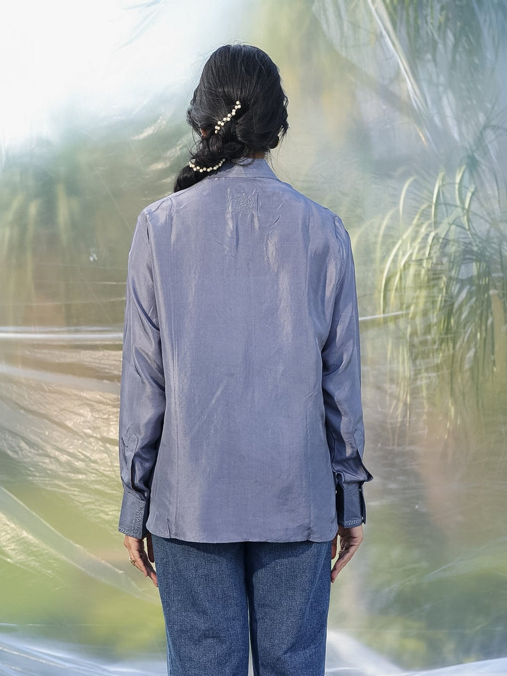 Person wearing a gray shirt and blue jeans standing in front of a plastic-wrapped landscape.