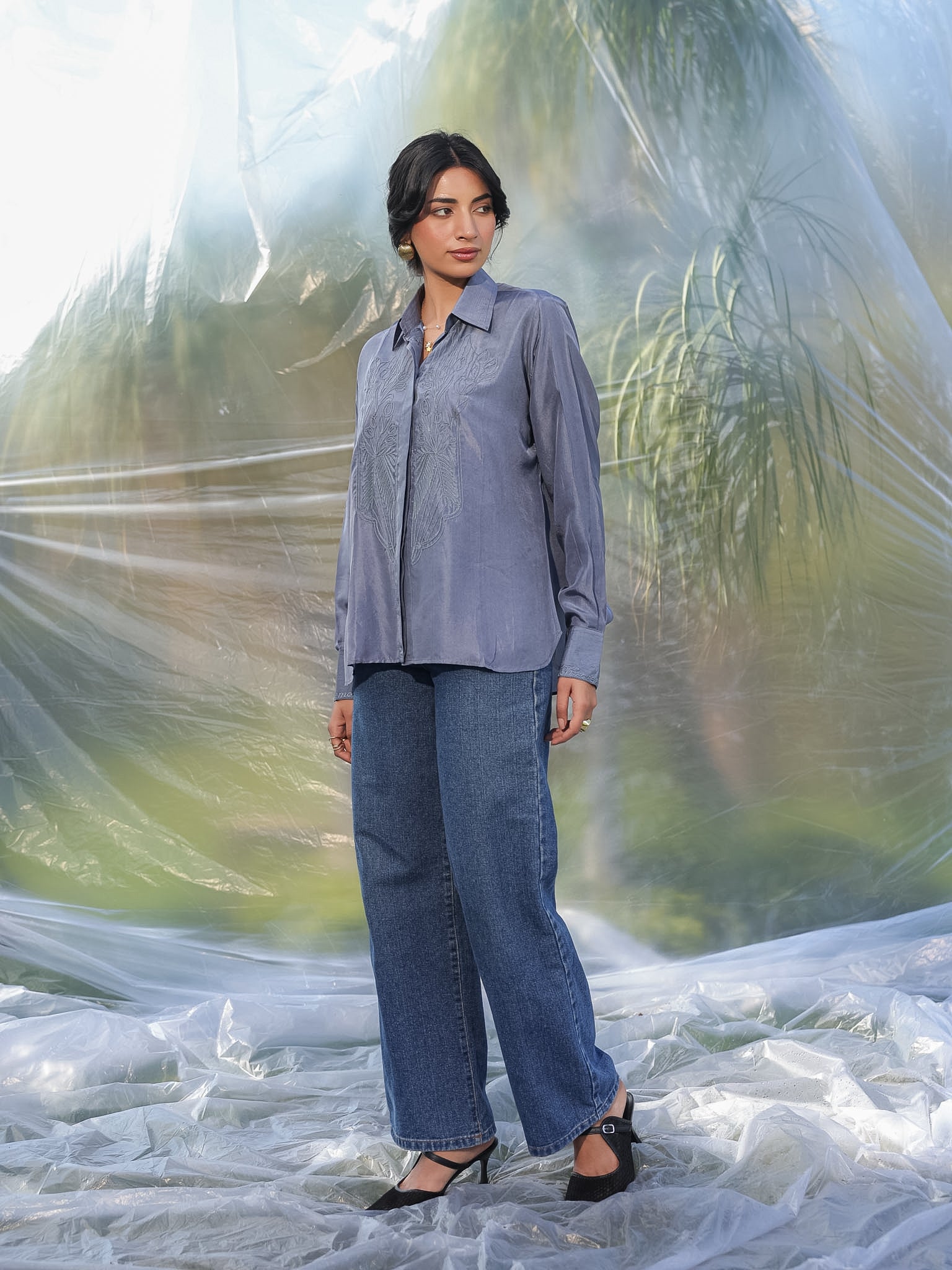 Person wearing a gray shirt and blue jeans standing against a textured white and green background
