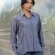 Woman wearing a grey shirt and jeans standing in front of a blurred natural background