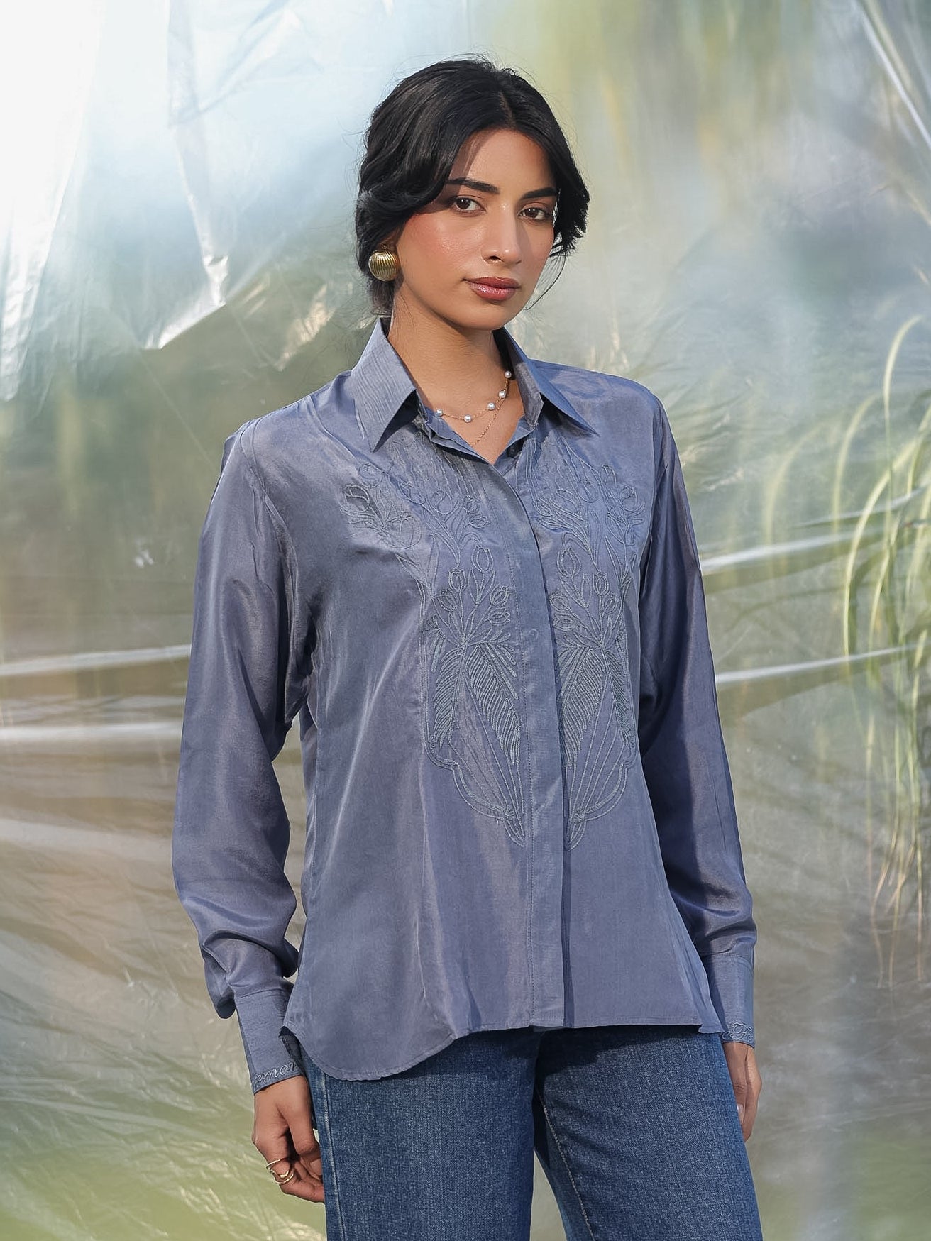 Woman wearing a grey shirt and jeans standing in front of a blurred natural background