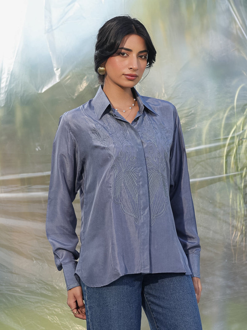 Woman wearing a grey shirt and jeans standing in front of a blurred natural background