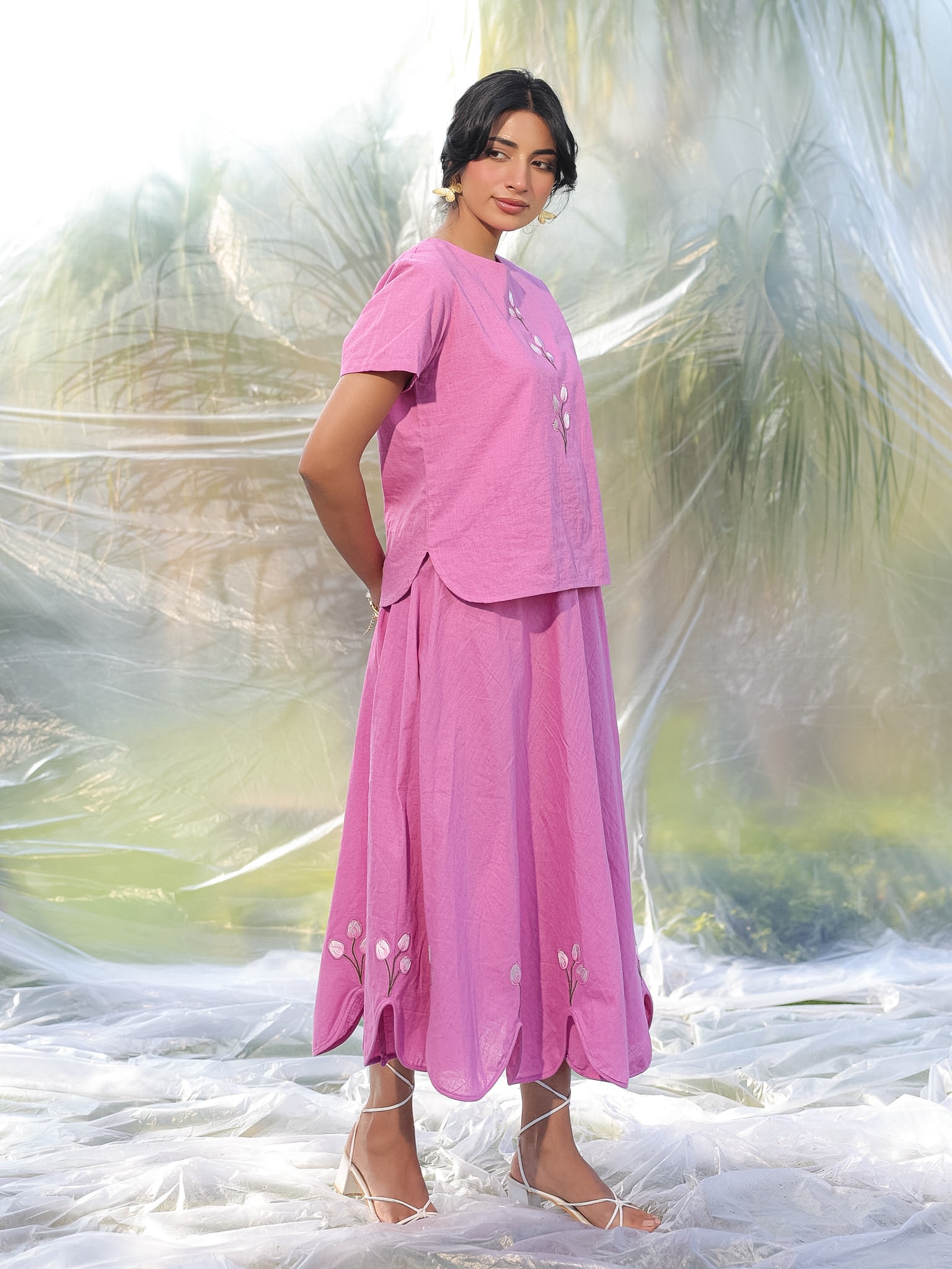 Woman wearing a pink top and skirt coord set with a blurred natural background