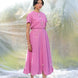 Woman wearing a pink top and skirt with floral details against a blurred natural background
