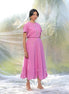 Woman wearing a pink top and skirt with floral details against a blurred natural background