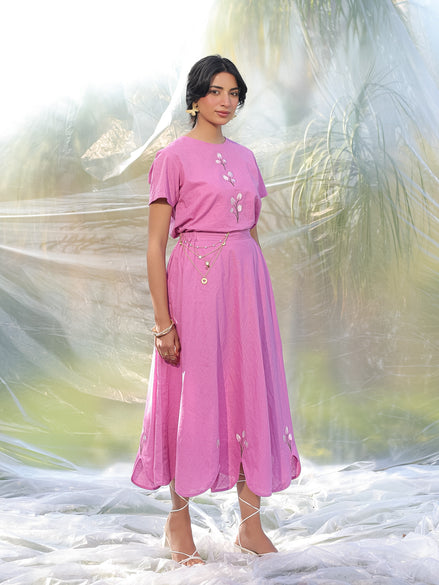 Woman wearing a pink top and skirt with floral details against a blurred natural background