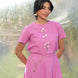 Woman wearing a pink cotton linen top and skirt with appliqued tulip embroidery against a blurred natural background