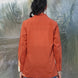 Person wearing a rust shirt and blue jeans standing in front of a textured wall.
