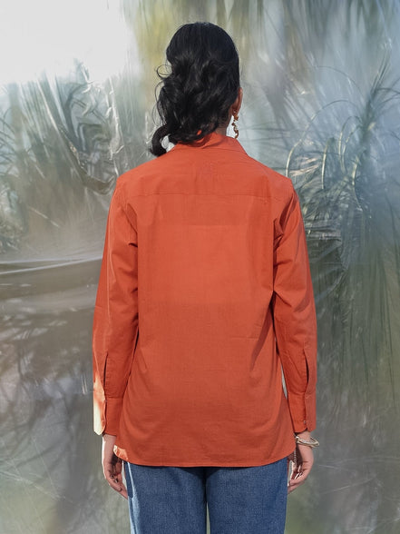 Person wearing a rust shirt and blue jeans standing in front of a textured wall.
