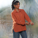 Woman wearing a rust orange shirt and blue jeans standing against a textured white background