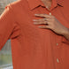 Person wearing a rust  orange textured shirt with quilted patch with a blurred background