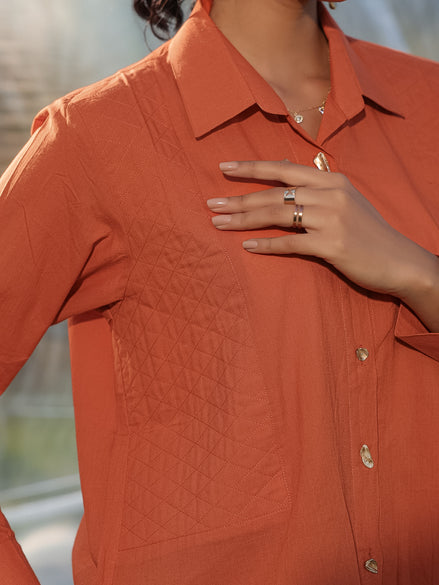 Person wearing a rust  orange textured shirt with quilted patch with a blurred background