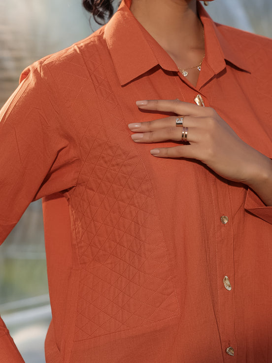 Person wearing a rust  orange textured shirt with quilted patch with a blurred background