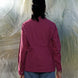 Person wearing a red wine shirt and blue jeans standing in front of a textured white wall.