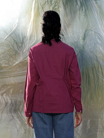 Person wearing a red wine shirt and blue jeans standing in front of a textured white wall.