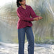 Woman wearing a maroonish wine shirt and blue jeans standing in front of a plastic sheet.