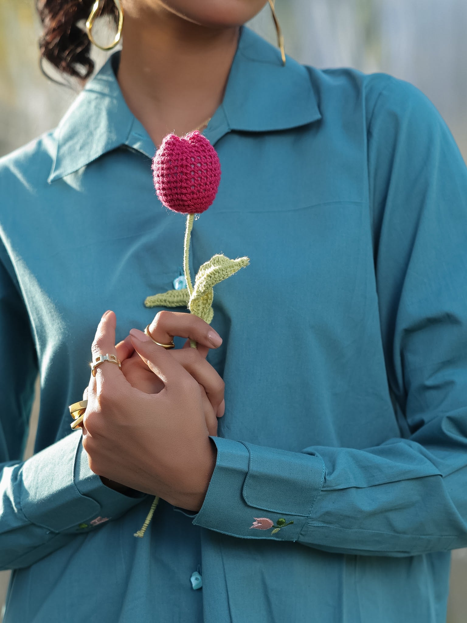 Person wearing a blue shirt holding a pink crocheted flower.