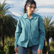 Woman wearing a teal shirt standing outdoors with palm trees in the background