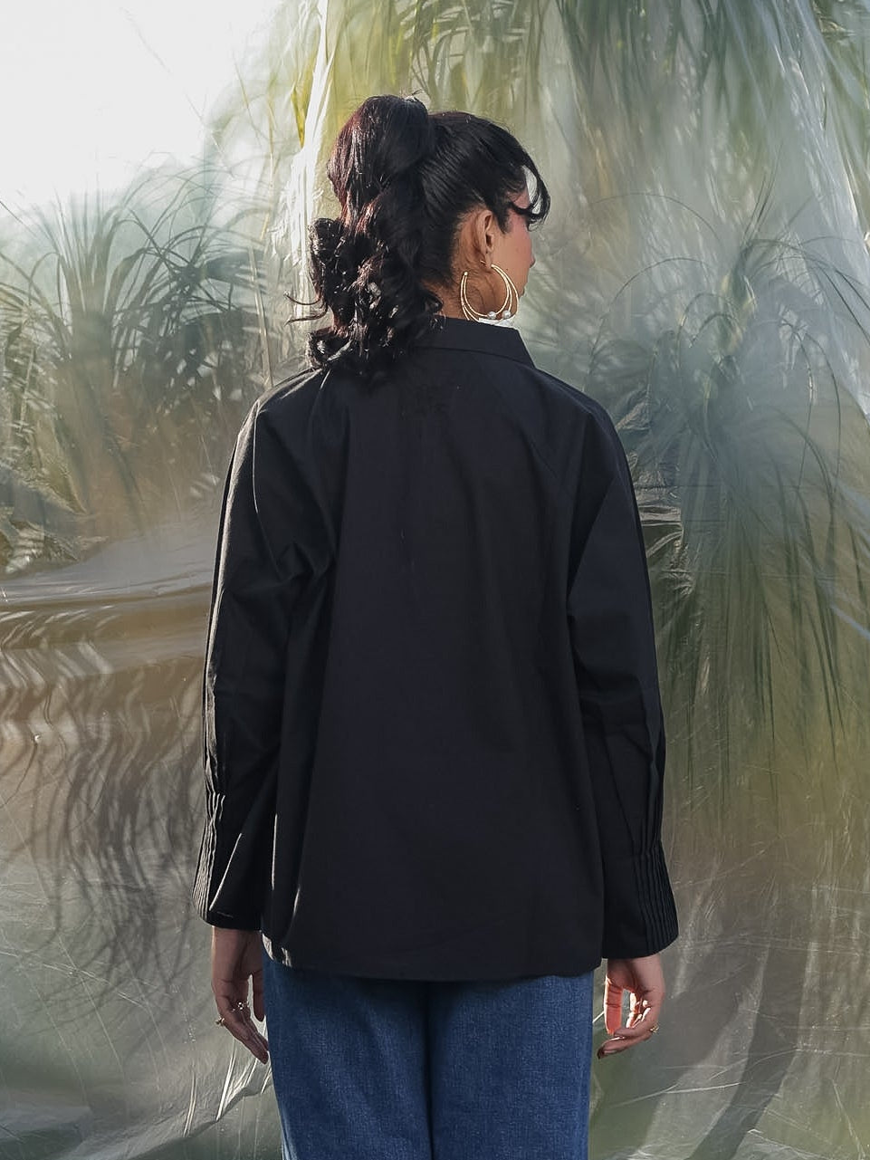 Person wearing a black shirt and blue jeans standing in front of a plastic-wrapped landscape.
