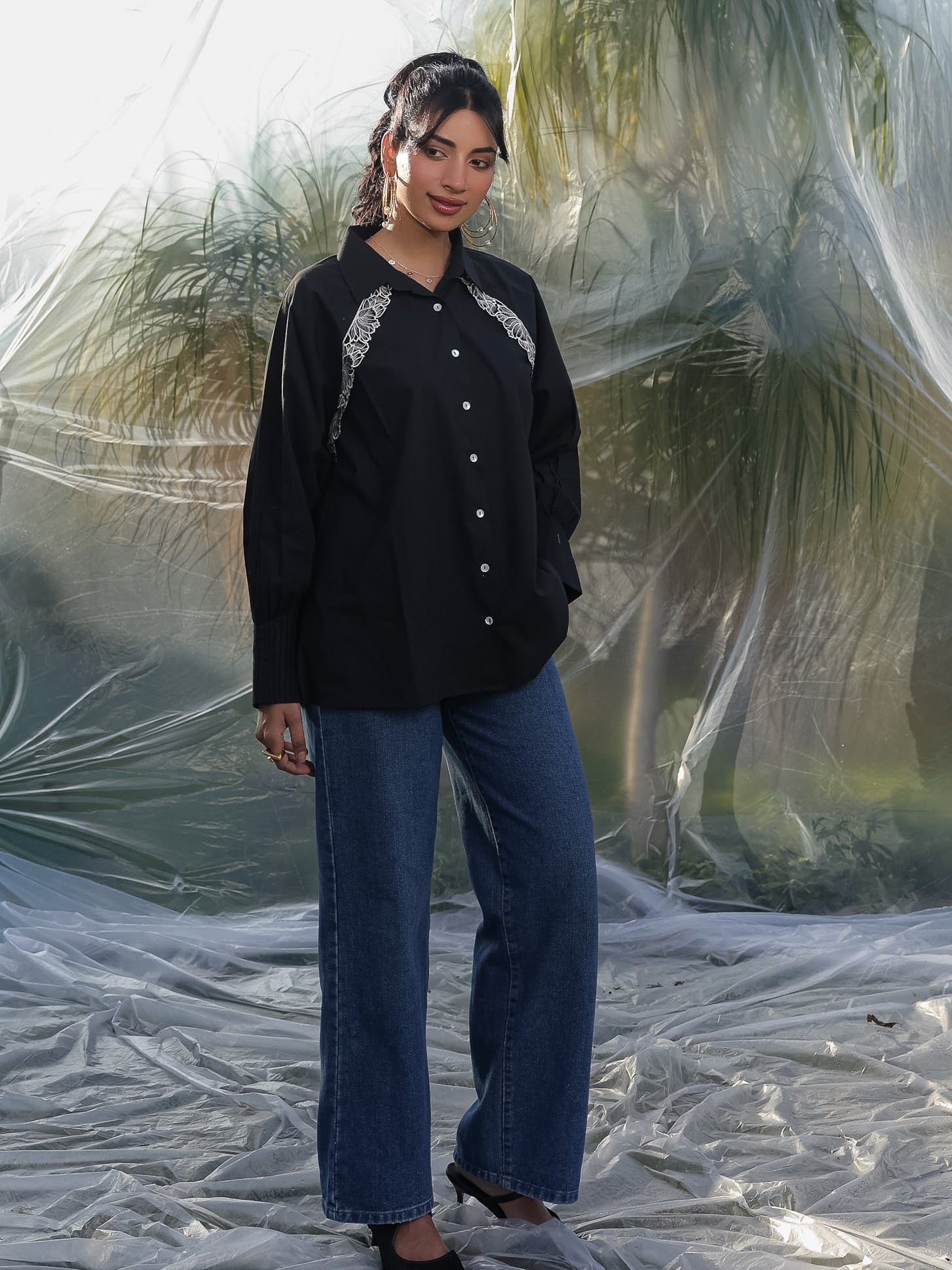 Person wearing a black shirt with white embroidery and blue jeans standing