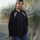 Woman wearing a black shirt with white embroidery standing against a transparent backdrop.
