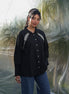Woman wearing a black shirt with white embroidery standing against a transparent backdrop.